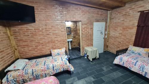 Habitación con 2 camas y TV en una pared de ladrillo. en Cabaña paisaje puntano Nogolí en Hipólito Yrigoyen