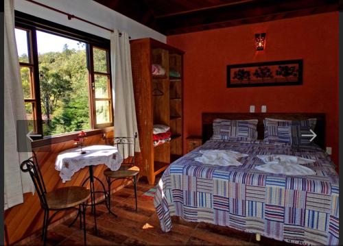 a bedroom with a bed and a table and a window at Pousada Brilho da Natureza in Visconde De Maua