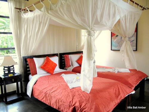 a bedroom with a canopy bed with red and white pillows at Bali Amber Villa in Banjar