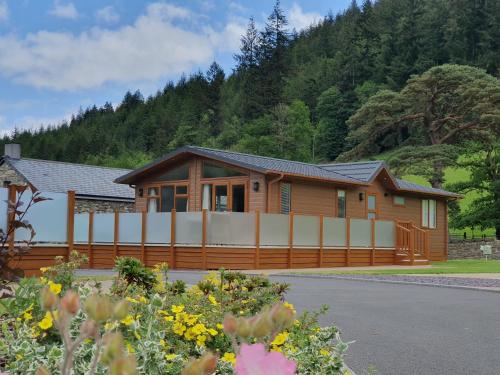 a wooden house with a fence and some flowers at Llyn Padarn Lodge in Betws-y-coed