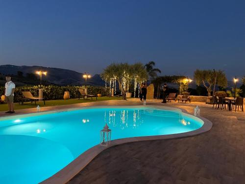 a blue swimming pool at night with people standing around it at Agriturismo Tenuta San Giovanni Casale Leto in SantʼAngelo Muxaro
