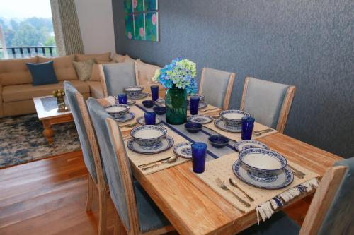 a wooden table with plates and a vase of flowers on it at Knightsbridge Grand Apartment in Nuwara Eliya
