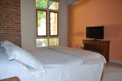 1 dormitorio con 1 cama blanca y TV en Coqueto departamento, Jardines del Rey en Neuquén