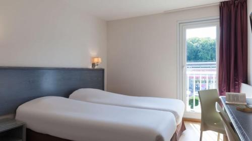 two beds in a hotel room with a window at The Originals City, Hôtel Le Louisiane, Belfort Sud (Inter-Hotel) in Andelnans