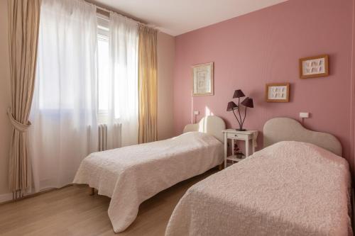ジョンザックにあるLaConciergerieJonzac, Maison de ville ALAMBICのピンクの壁と窓が特徴の客室で、ベッド2台が備わります。