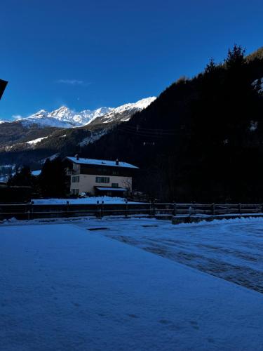 un campo cubierto de nieve con una casa y montañas en Bianchina - Bilocale con giardino privato en Valdisotto