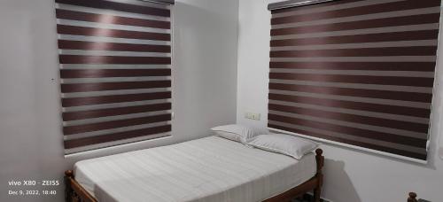 a small bed in a room with two windows at Oman house 2.O in Ernakulam