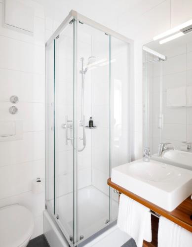 a white bathroom with a shower and a sink at Hotel Haus am See in Nonnenhorn