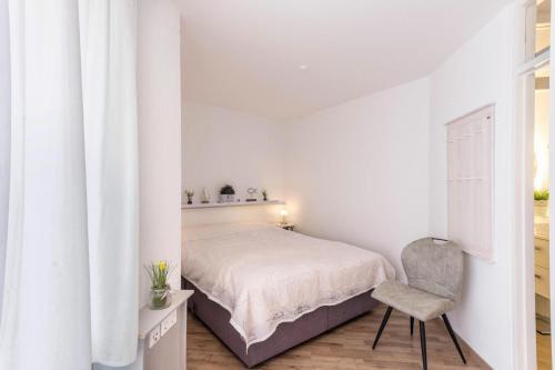 a white bedroom with a bed and a chair at Am Horumertief in Wangerland
