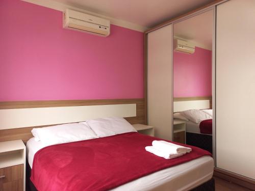 um quarto com paredes cor-de-rosa e uma cama com um cobertor vermelho em Residencial Nicole em Florianópolis