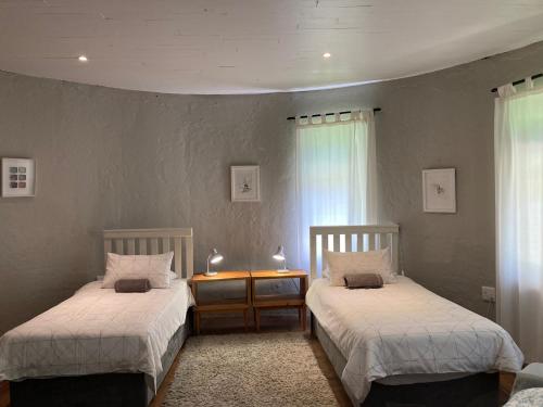 a bedroom with two beds and a table and windows at Bramber Cottage Hogsback, Living With Joy! in Hogsback