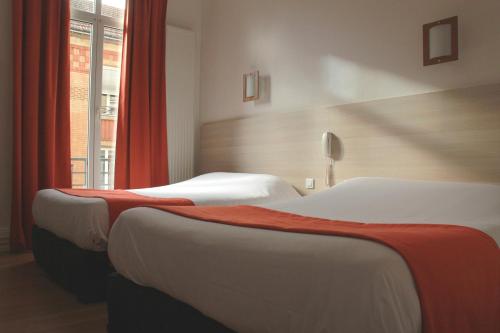 two beds in a hotel room with a window at Hôtel De La Cathédrale in Reims