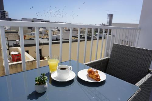 een tafel met een kopje koffie en croissants op een balkon bij KORZO SUITES in Il-Gżira
