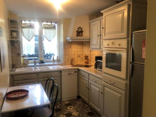 - une cuisine avec des placards blancs, un évier et une table dans l'établissement La Glycine, à La Canourgue