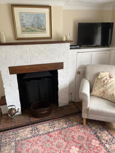 a living room with a fireplace with a chair and a television at Field Cottage in Whittlesey