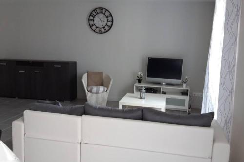 un salon avec un canapé blanc et une horloge au mur dans l'établissement La maison d'Emmanon, à Saint-Saturnin-du-Bois