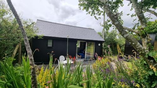 a black tiny house in the middle of a garden at Hallegan Annexe with Private Garden and Woodland in Camborne