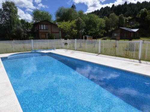 a blue swimming pool with a fence and a house at Balcones de Puelo in Lago Puelo