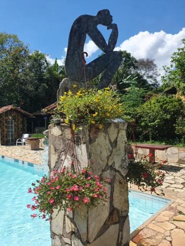 a statue sitting next to a swimming pool with flowers at Capricho Asturiano in Santo Antônio do Leite