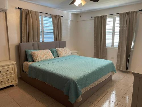 a bedroom with a bed with a blue blanket and windows at Beautiful Villa 5 mins from Crash Boat Aguadilla 1 in Aguadilla