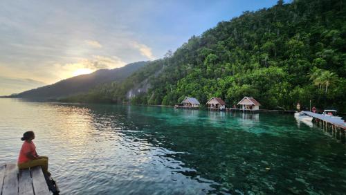 una mujer sentada en un muelle en un lago en Terimakasih homestay, en Pulau Mansuar