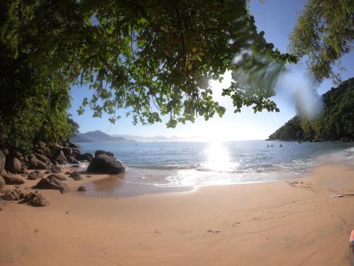una spiaggia con il sole che splende sull'acqua di APTO PERTINHO DA PRAIA - Lindo e Equipado! Internet 400mb e 3 Tvs - Completo! TV a Cabo a Ubatuba