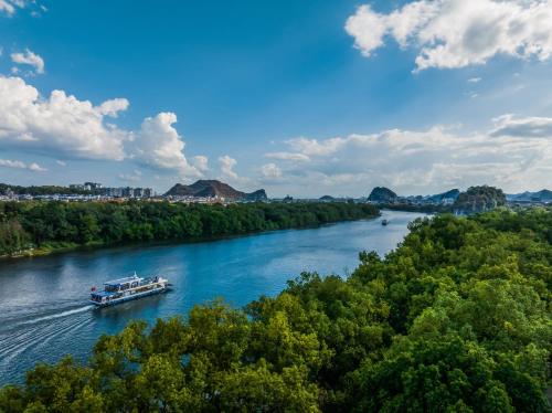 a boat traveling down a river with trees at Wing Hotel Guilin - Central Square in Guilin