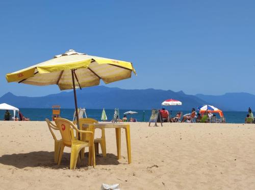 einen Tisch und Stühle unter einem Sonnenschirm am Strand in der Unterkunft Recanto Dubay in Caraguatatuba