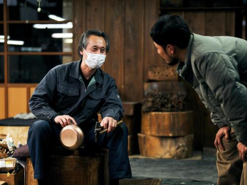 a man wearing a mask sitting on a barrel while another man is standing at SNOW PEAK FIELD SUITE SPA HEADQUARTERS in Morimachi