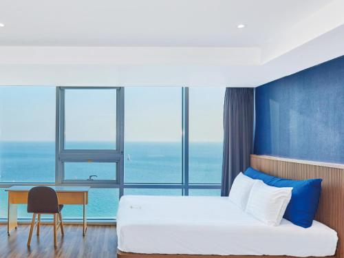 ein Hotelzimmer mit einem Bett, einem Schreibtisch und Fenstern in der Unterkunft Kolon Seacloud Hotel in Busan