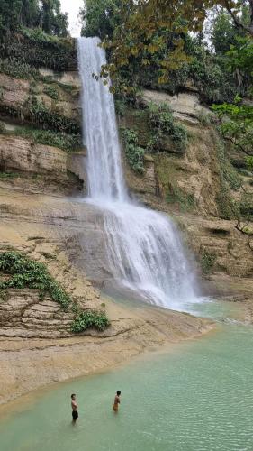 two people in the water in front of a waterfall at LHOYJEAN Garden Hostel in Batuan