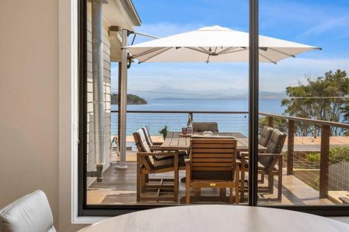 a dining table with chairs and an umbrella on a balcony at 'The Alonnah' Beach House - Main House & Unit in Alonnah
