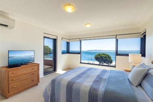 a bedroom with a bed and a tv and windows at Florentine 14 - 11 Columbia Close Aircon Wifi unsurpassed water views in Nelson Bay