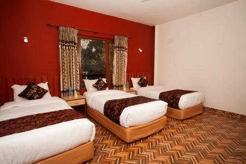 a hotel room with three beds with red walls at Sauraha Holiday Home Riverside in Chitwan