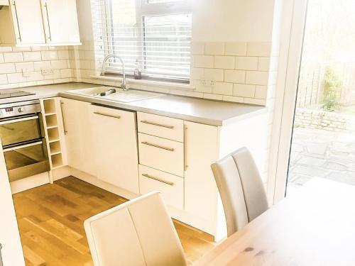 uma cozinha com armários brancos e uma mesa e cadeiras em 3-Bed House in London Garden & free parking em Dartford