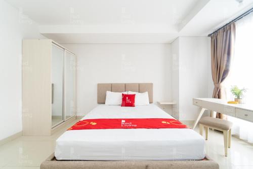 a white bedroom with a large bed with a red blanket at RedLiving Apartemen Barsa City by Ciputra - WM Property in Yogyakarta