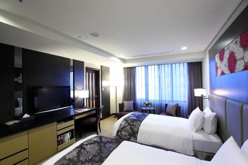 a hotel room with two beds and a flat screen tv at Golden Tulip Zhong Xin Hotel Taichung in Taichung