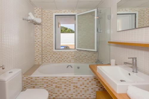 a bathroom with a tub and a toilet and a sink at Villa Jamaica in Fornells