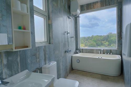 ein Bad mit einer Badewanne, einem WC und einem Fenster in der Unterkunft Kandyan Mount Mirror Boutique Villa in Kandy