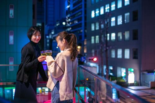 two women standing on a balcony in a city at night at The Royal Park Canvas - Osaka Kitahama in Osaka