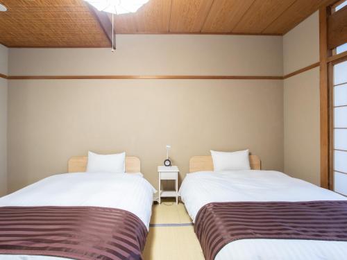 two beds in a room with white walls and wooden ceilings at Tabist Hotel Chouseikaku in Yatsushiro