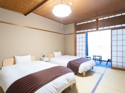 a bedroom with two beds and a large window at Tabist Hotel Chouseikaku in Yatsushiro