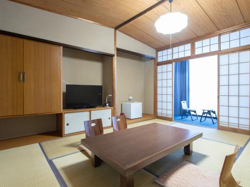 a living room with a wooden table and a tv at Tabist Hotel Chouseikaku in Yatsushiro