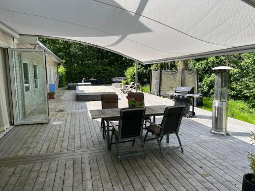 een patio met een tafel en stoelen onder een witte parasol bij Lugn och lummig oas för den stora familjen, söndag -söndag in Båstad