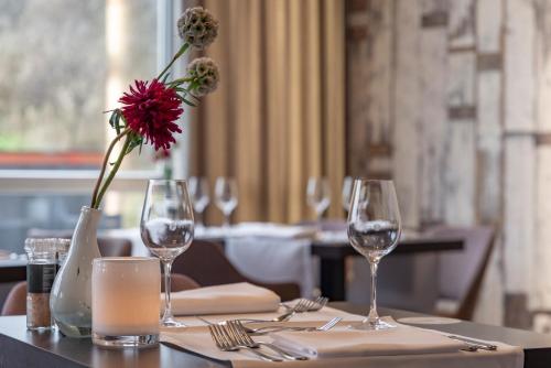 a table with wine glasses and a vase with a red flower at Fletcher Hotel Restaurant Zeeduin in Wijk aan Zee