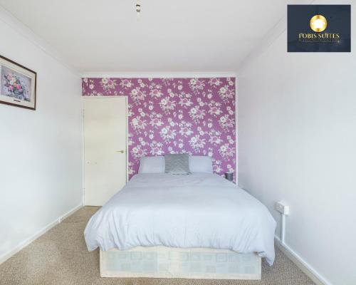1 dormitorio con cama blanca y papel pintado con motivos florales en Fobis Suites Short Lets for 3 Bed Family Group Contractors Dagenham, en Dagenham