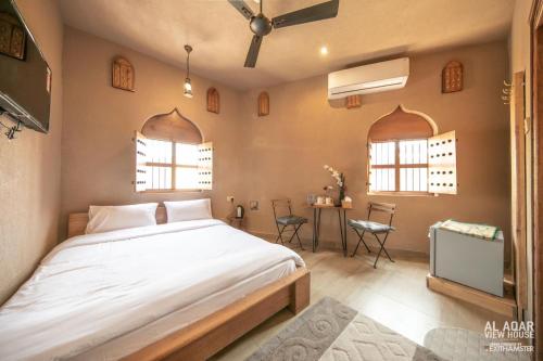 a bedroom with a bed and a table and two windows at Alaqur View Inn نزل واجهة العقر in Nizwa