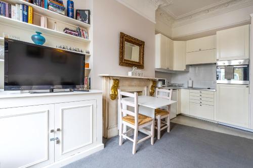 cocina con armarios blancos, mesa y TV en Bright 2 bedroom flat with terrace in Notting Hill, en Londres