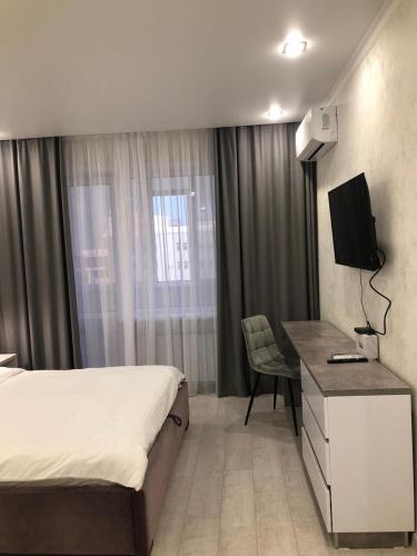 a bedroom with a bed and a desk with a television at Новая современная квартира в центре города in Kostanay