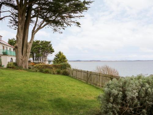 a yard with a fence and a tree next to the water at Rocklea Seaside Cottage in Newcastle